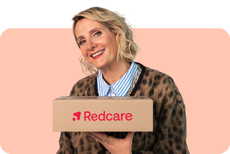 Une femme souriante en vêtements à motifs tient un colis avec le logo Redcare devant un fond rose.